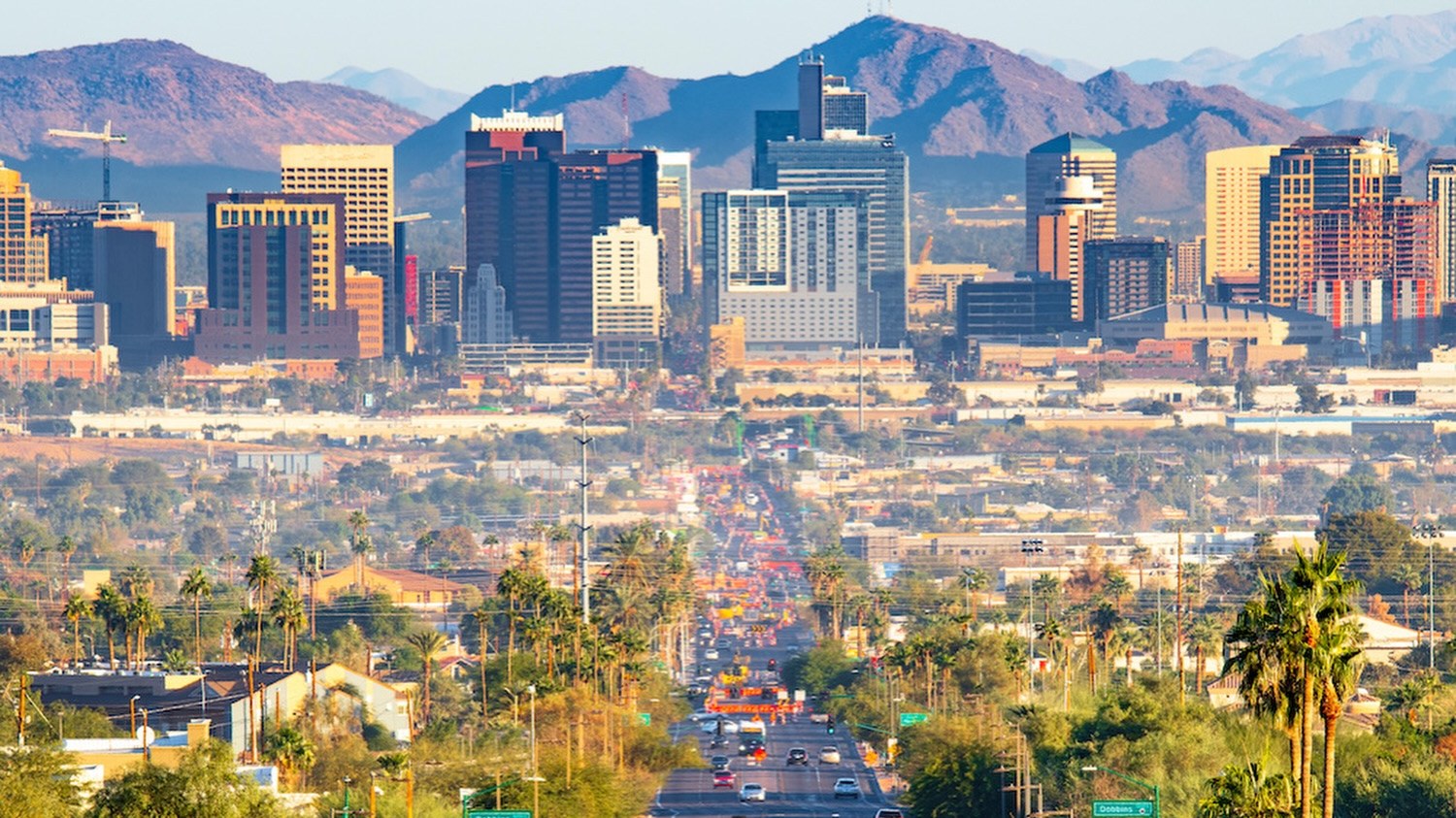 Palm lined avenue leading to the downtown Phoenix skyline with mountains behind